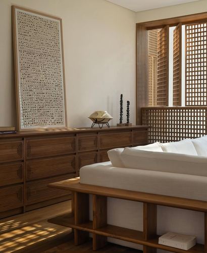 Bedroom corner with carved wood dresser, lattice screen window, and white upholstered bed bench