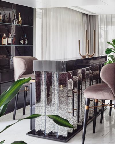 Mirrored fluted bar counter with marble top and mauve velvet stools in a Mumbai residence