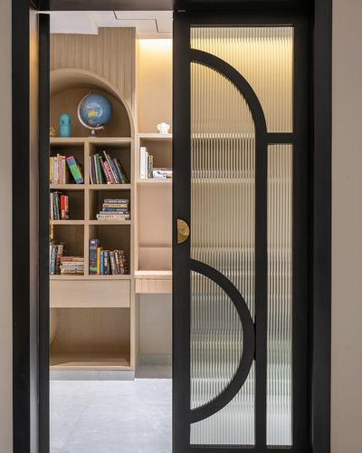 Black-framed fluted glass door opens to an arched wooden study nook with bookshelves and globe