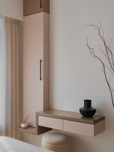 Pink floating console with black vase beside a tall wardrobe with black handle in a minimalist bedroom corner