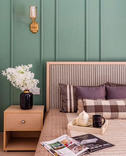 Bedroom corner with sage green paneled wall, striped headboard, brass sconce and styled nightstand