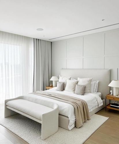 Neutral bedroom with upholstered bed, curved bench, and sheer curtains beside window