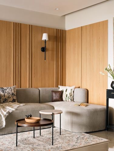Grey sectional sofa against fluted wood paneled corner wall with wall sconce and round coffee tables