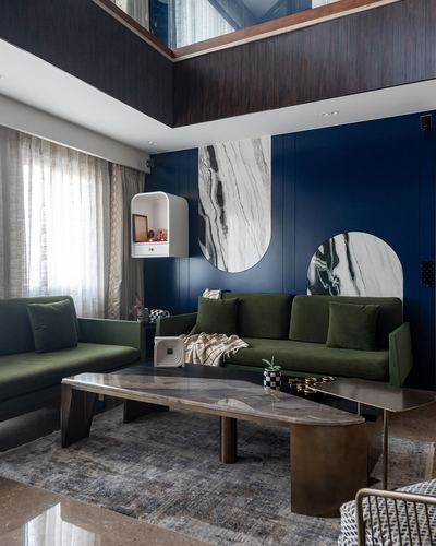 Double-height living room with navy panelled wall, marble circular insets, and green velvet sofas