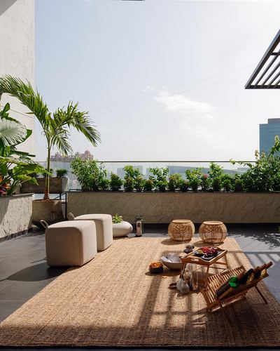 Rooftop terrace lounge with jute rug, cane stools, and city skyline view in daylight