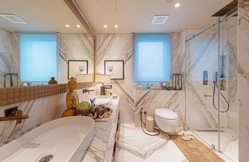 Luxury bathroom with marble-look tile walls, dual vanity, gold fixtures, and glass shower