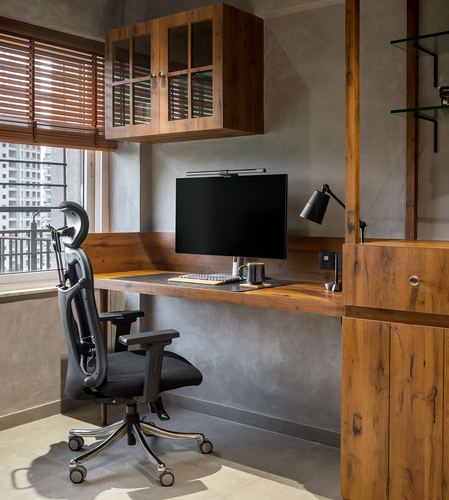 Wooden home office desk with monitor, lamp, and black ergonomic chair against textured grey wall