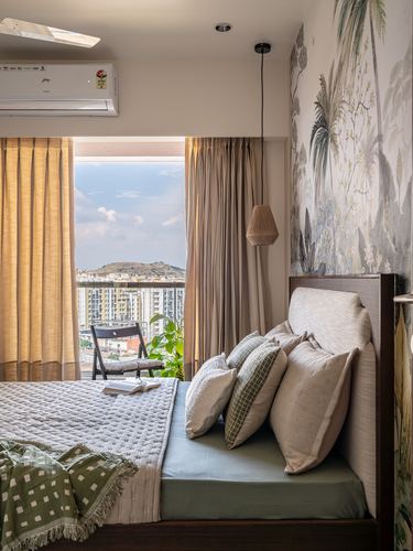 Bedroom with botanical mural wall, cane pendant light, and city skyline view through curtained window