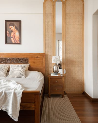 Wooden bed with carved headboard beside arched cane wardrobe panels and nightstand