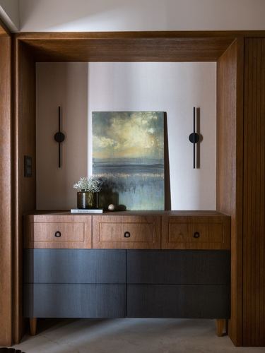 Wood-framed niche with ribbed cabinet, artwork, and sconces in a foyer