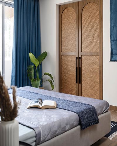 Bedroom with arched cane wardrobe doors, blue curtains, and a bed dressed in grey and indigo linens