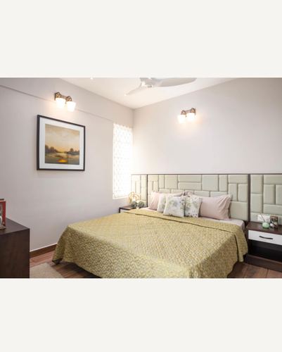 Bedroom with tufted cream headboard, mustard bedspread, wall sconces, and framed landscape print