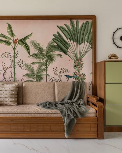 Wooden daybed with beige cushions against a botanical mural panel, marble floor, sage cabinet beside it