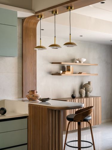 Kitchen counter with fluted wood island, brass pendant lights, and floating shelves against textured wall