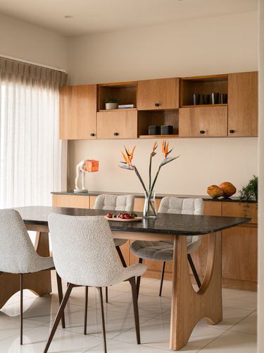 Dining room with wood table on sculptural base, boucle chairs, and wall cabinetry with open shelving.