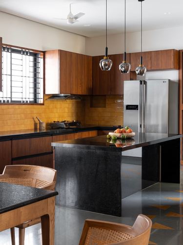 Wood-cabinet kitchen with mustard tile backsplash, black stone island, and hanging glass pendant lights