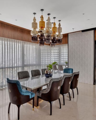 Dining room with marble table, mixed velvet and leather chairs, and cluster bottle chandelier against sheer-curtained windows