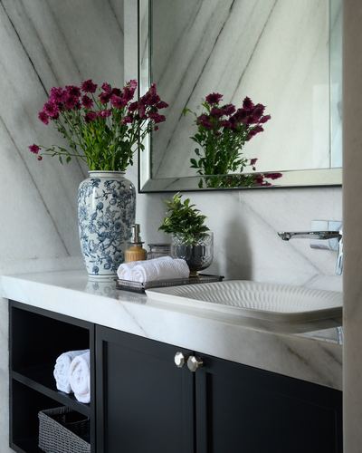 Marble bathroom vanity with fluted basin, navy cabinetry, and vase of pink flowers