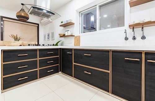 L-shaped kitchen with black wood cabinetry, brass trim, white countertop and open shelving