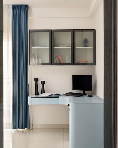 Compact study nook with pale blue curved desk, glass-front cabinet, and monitor