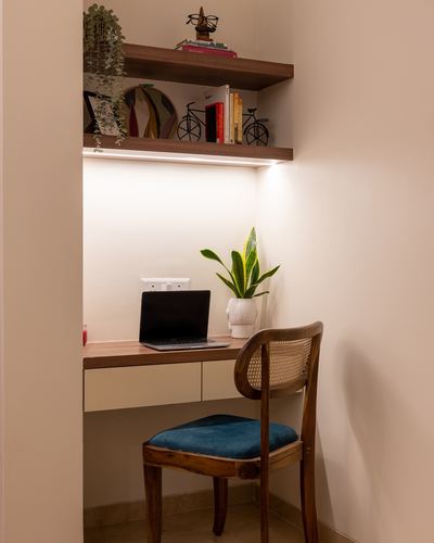 Small study nook with floating desk, laptop, plant, and cane-back chair with teal seat