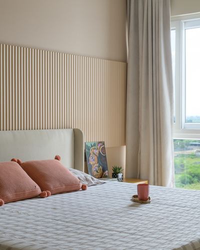 Bedroom with fluted wood headboard wall, terracotta cushions, and daylight through sheer curtain