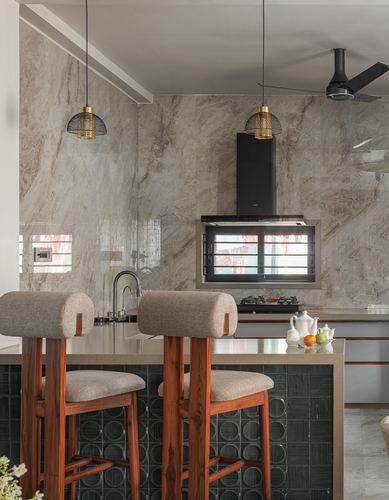 Kitchen island with wooden stools and green tiled base beneath stone-clad wall and black chimney hood