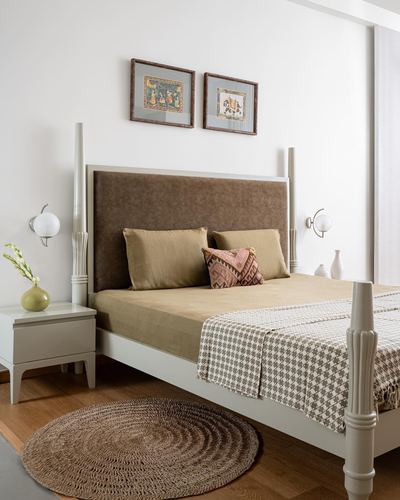 Bedroom with carved four-poster bed, olive linens, framed miniatures, and round jute rug