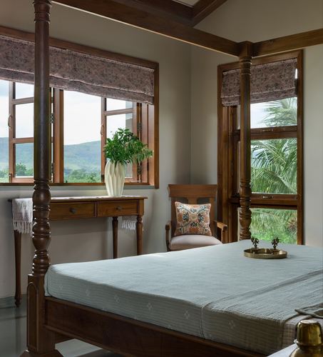 Teak four-poster bed in farmhouse bedroom with windows overlooking hills and palms