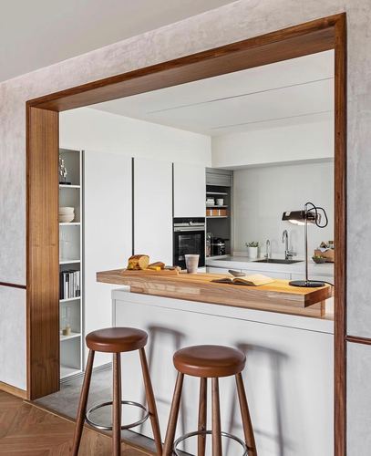 White kitchen with wood breakfast counter and leather stools seen through a timber-framed doorway