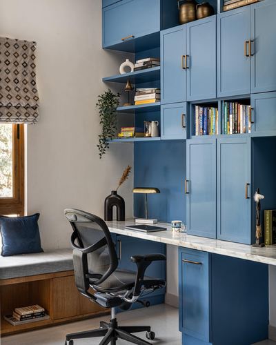 Home study with blue built-in cabinetry, marble desk, mesh office chair and window seat