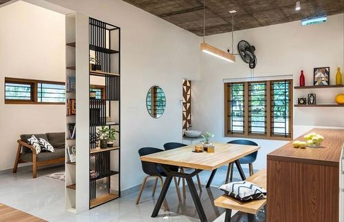 Open-plan dining area with wooden table, black chairs, slatted shelf divider and exposed concrete ceiling