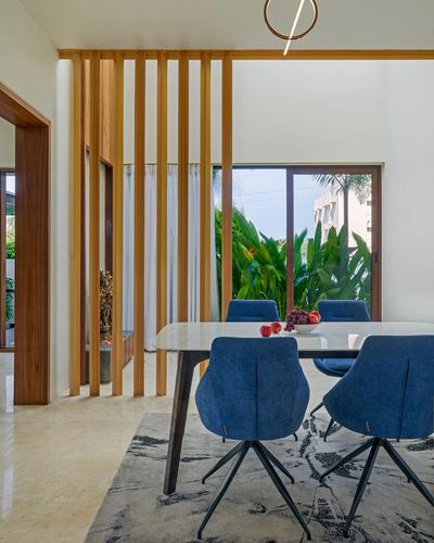 Dining table with blue chairs beside timber slat screen and green view
