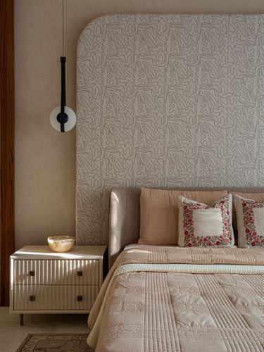 Bedroom with curved patterned headboard wall, pendant light, and fluted nightstand with embroidered cushions on bed