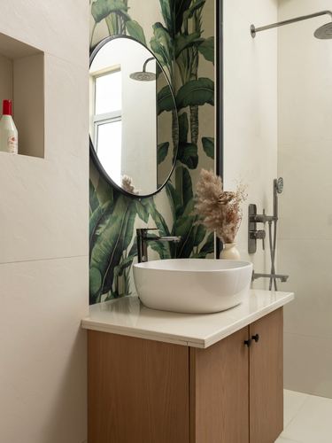 Bathroom vanity with round mirror, banana leaf wallpaper, white vessel sink and wood cabinet