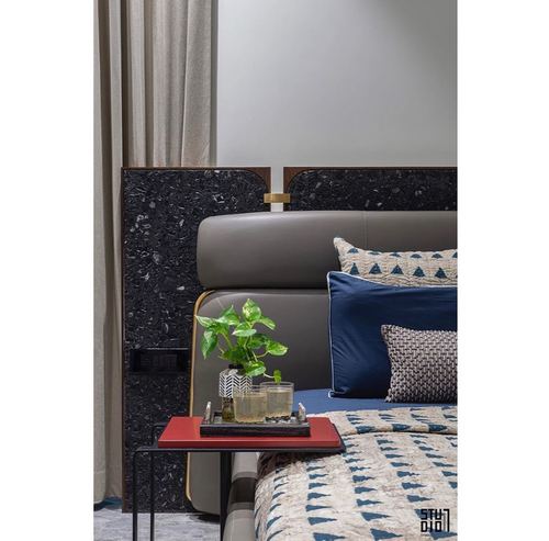 Bedroom corner with stone-clad headboard, leather backrest, patterned pillows, and a red side table.