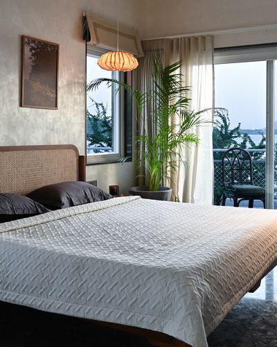 Bedroom with cane headboard, quilted bedcover, pendant light, and balcony overlooking a lake