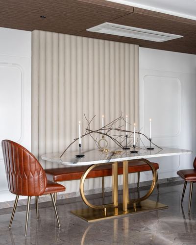 Dining table with marble top and gold oval base, rust leather chairs, fluted panel backdrop
