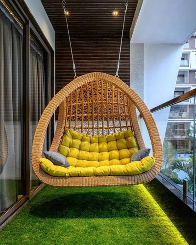 Woven hanging egg swing with yellow cushions over artificial turf on a high-rise balcony