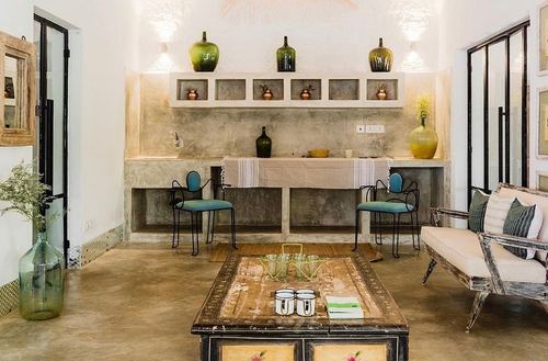 Rustic living room with plastered niche wall, glass bottles, teal metal chairs, and a distressed wooden coffee table