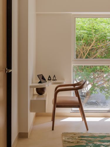Sunlit study nook with wooden armchair, floating desk, and window overlooking trees