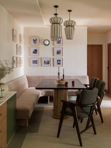 Dining nook with pink banquette, wood table, dark chairs, and gallery wall under pendant lanterns