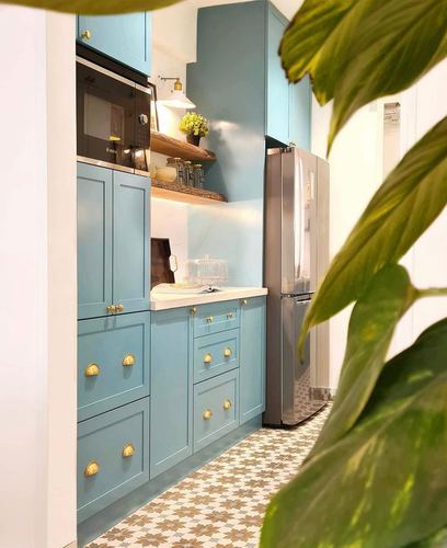 Dusty blue shaker kitchen with brass knobs, patterned floor tiles and open wood shelf
