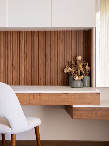 Study nook with fluted wood panel backdrop, floating wood desk, white chair, and decorative vases