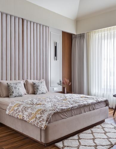 Bedroom with channel-tufted blush headboard wall, floral quilt, and sheer curtained window.