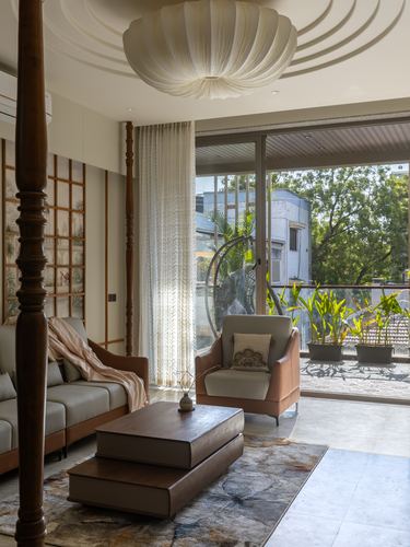 Living room with carved wooden post, layered wood coffee table, sheer curtains and balcony view of trees