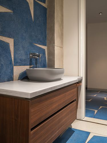Bathroom vanity with grey stone basin on white countertop against blue star-patterned terrazzo wall