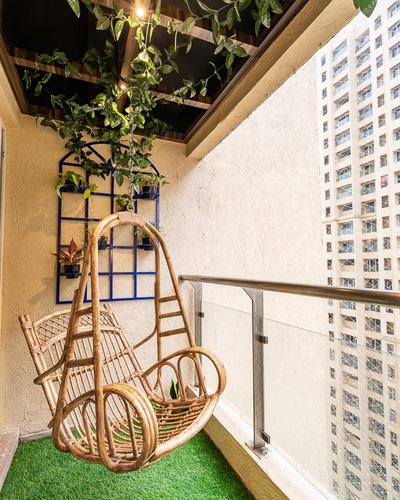 Rattan hanging swing chair on a balcony with vines, turf flooring, and city skyline view