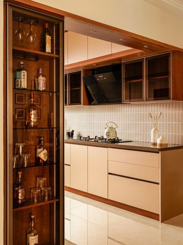 Open kitchen with wood-trimmed cabinetry beside a glass bar display shelf stocked with bottles and glassware