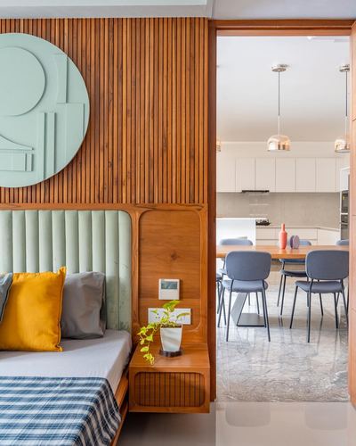 Bedroom with fluted wood wall and green disc art opening to a dining and kitchen area beyond